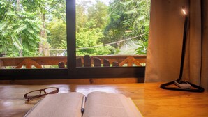 An open book on a wooden table with a pair of glasses beside it, near a window with a view of lush greenery. - Treehouse in the Canopy close to beach - large garden with trails - Pavones wave (Pavones)