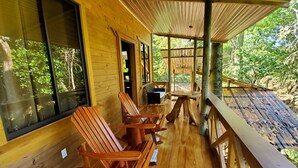 A wooden deck with wooden chairs and a table, surrounded by glass windows offering a view of the forest. - Treehouse in the Canopy close to beach - large garden with trails - Pavones wave (Pavones)