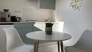 Cocina moderna con estufa integrada, cafetera y lavaplatos. Hay una pequeña mesa con sillas y una planta en maceta.