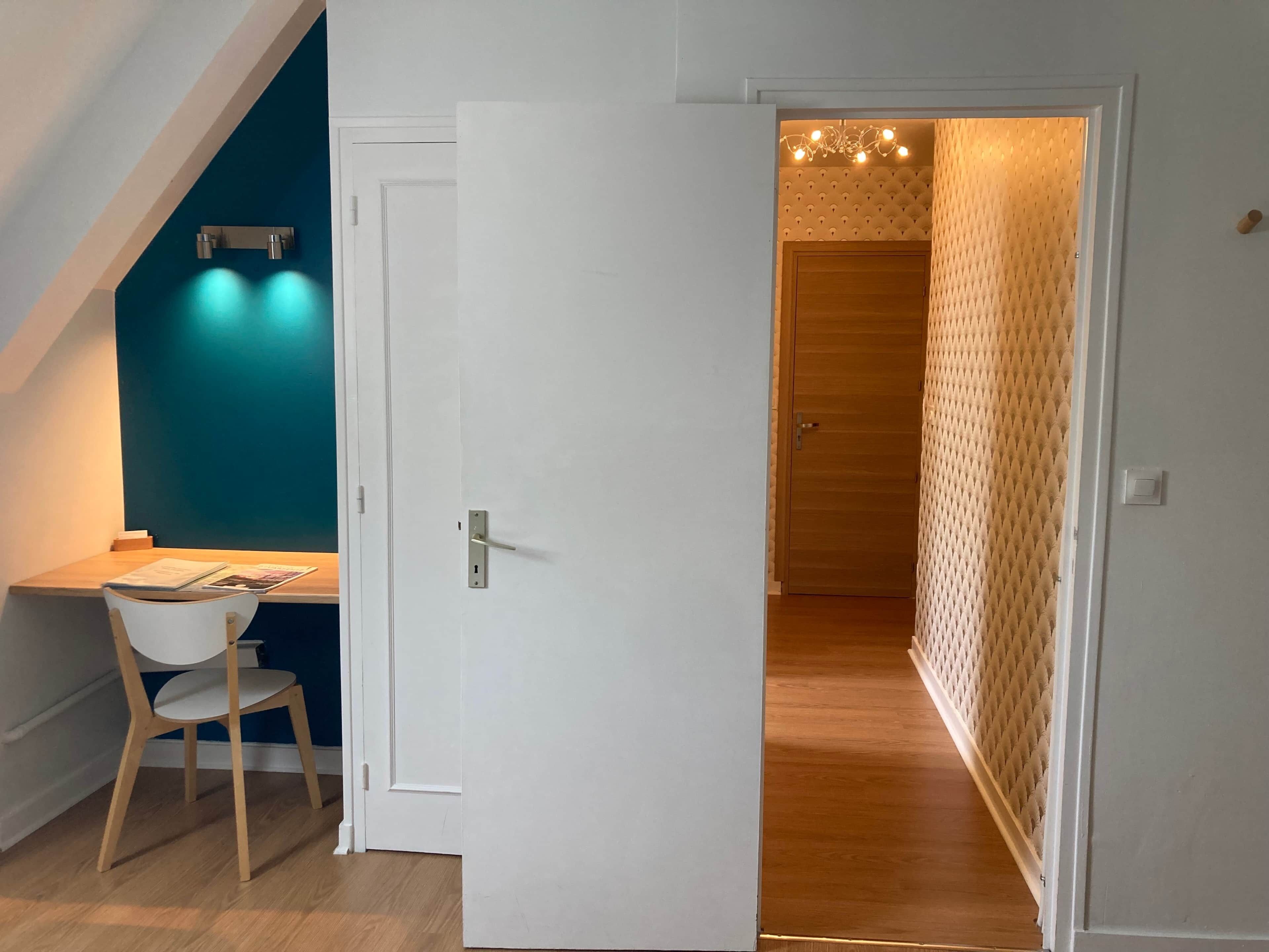 A room with a white door, a desk with a chair, a blue wall, and a wooden door in the background.