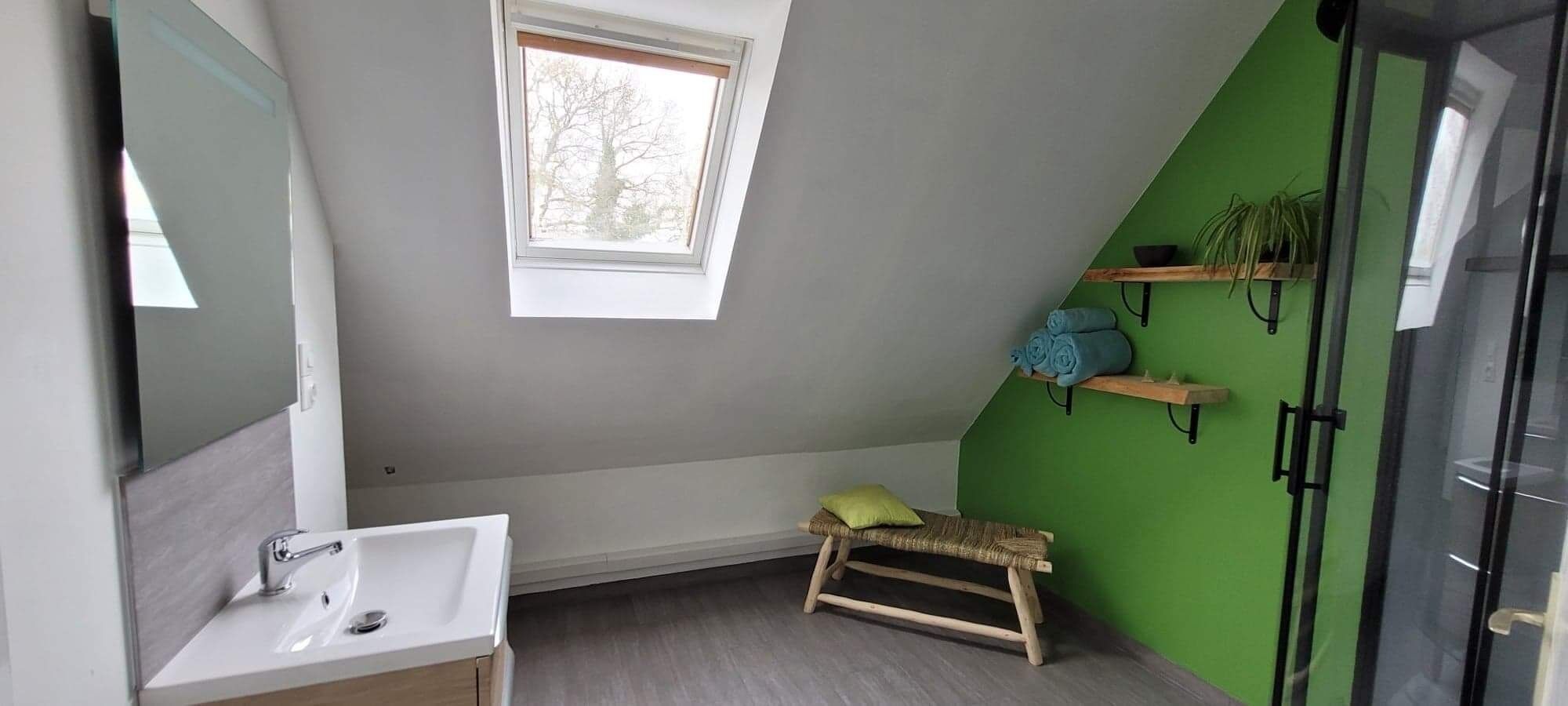 Une salle de bain moderne dotée d’un puits de lumière, d’un banc en bois et d’un mur d’accent vert.