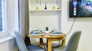 Comedor con una mesa redonda, dos sillas y un televisor en la pared mostrando una pantalla de selección de perfil.