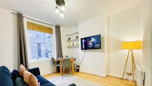 Una sala de estar moderna con un sofá, una mesa de comedor, un televisor montado en la pared y una lámpara de pie.