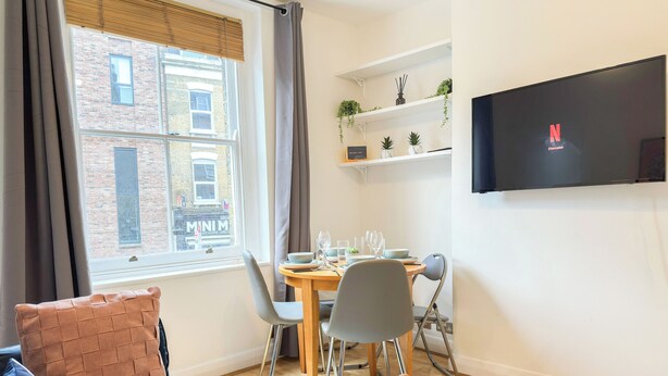 Una sala moderna con un sofá, una mesa de comedor para dos personas y un televisor en la pared.