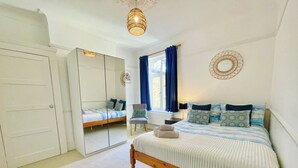 Un dormitorio con cama, una silla, armario y ventana con cortinas.