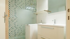 A bathroom with a checkered tile wall, a glass shower enclosure, a white sink, and a mirror above the sink.