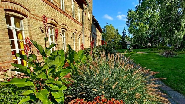 Een bakstenen gebouw met grote ramen en een verzorgde tuin met diverse planten en bloemen.