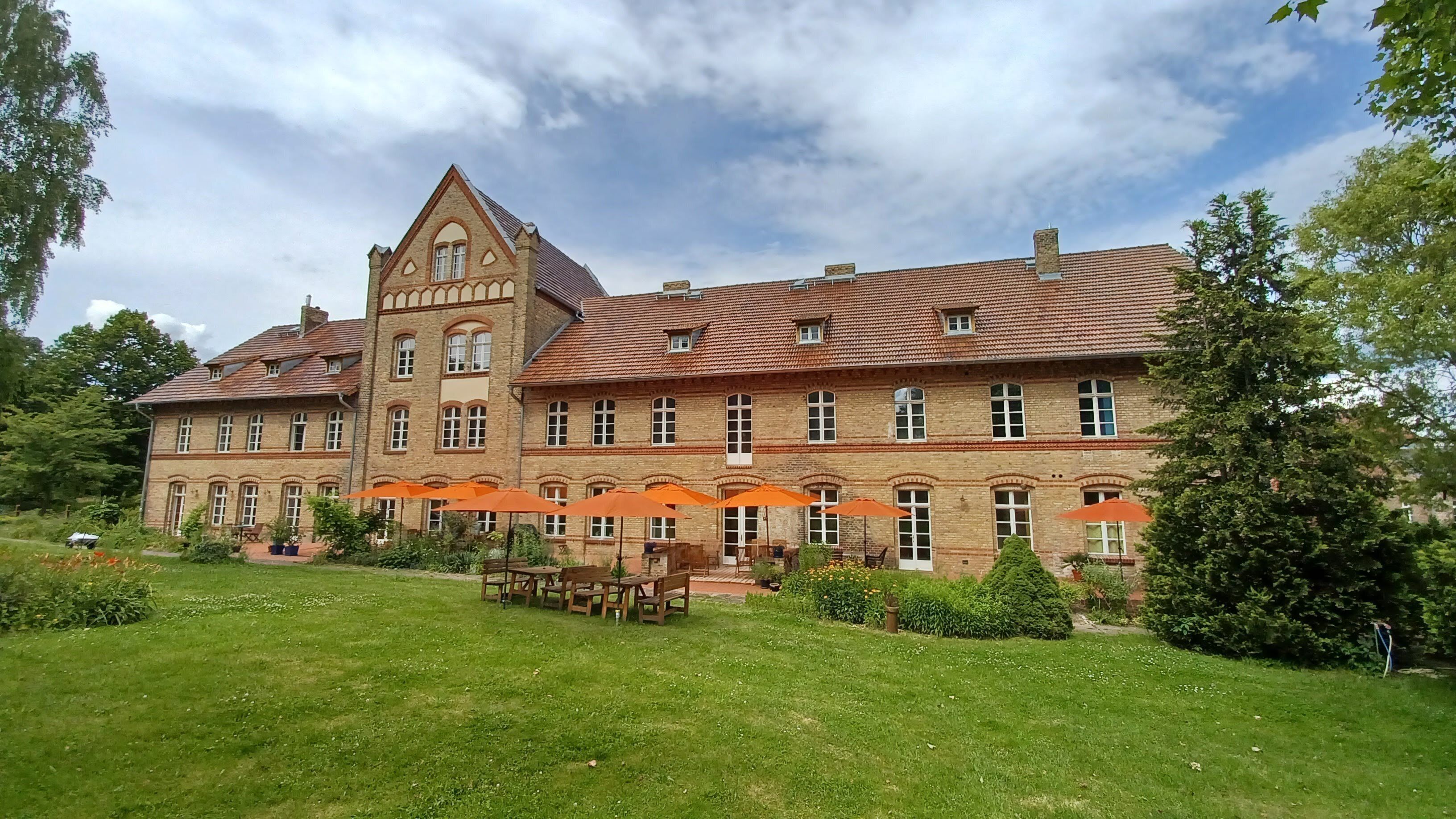 Un edificio grande e histórico con una torre destacada, numerosas ventanas y un jardín bien cuidado con asientos al aire libre.