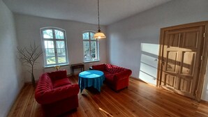 Een kamer met twee rode fauteuils, een kleine ronde tafel en een houten deur.