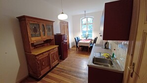 Een kleine keuken met houten kastjes, een koelkast, een eettafel met stoelen en een raam met uitzicht.