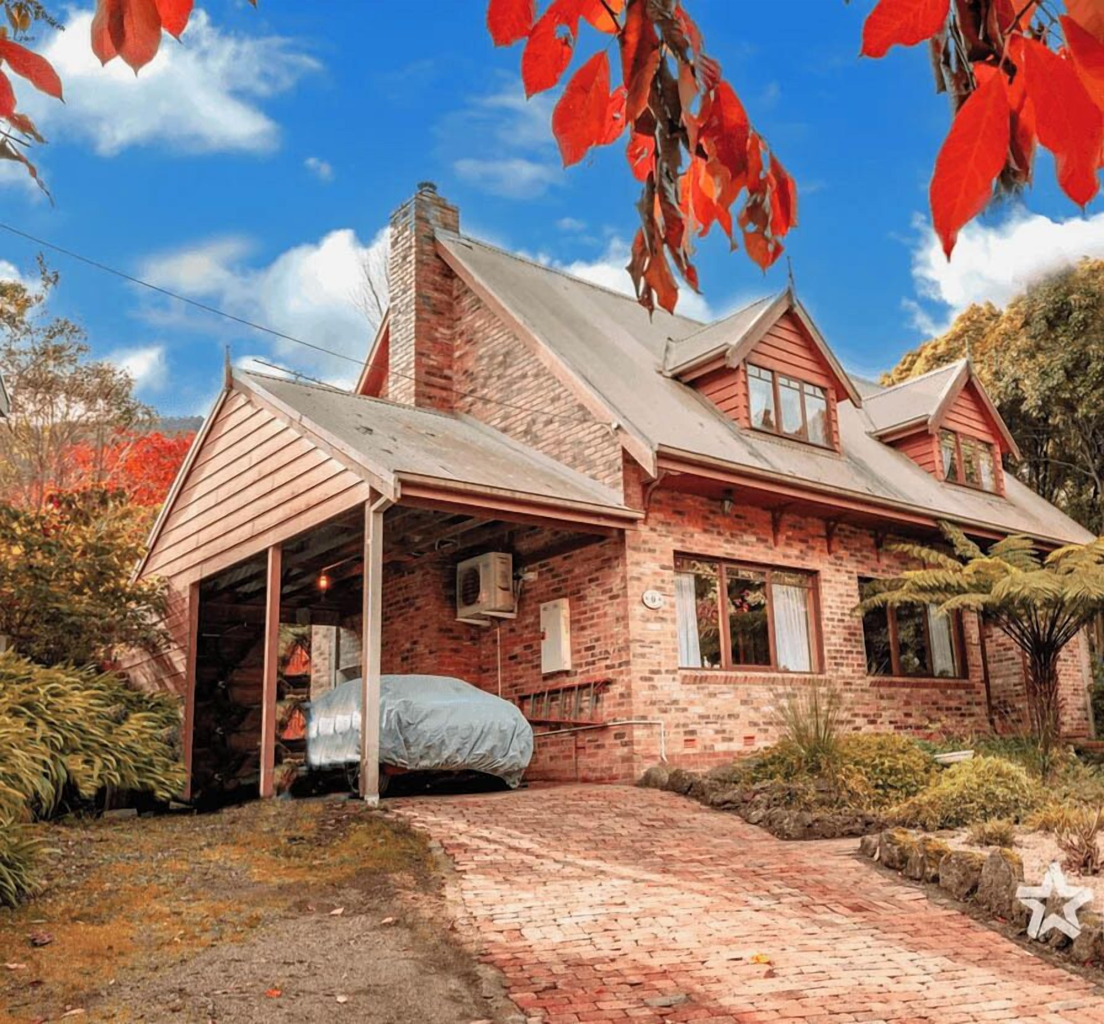 Una casa a due piani in mattoni con un portico coperto e un'auto coperta da un telo.