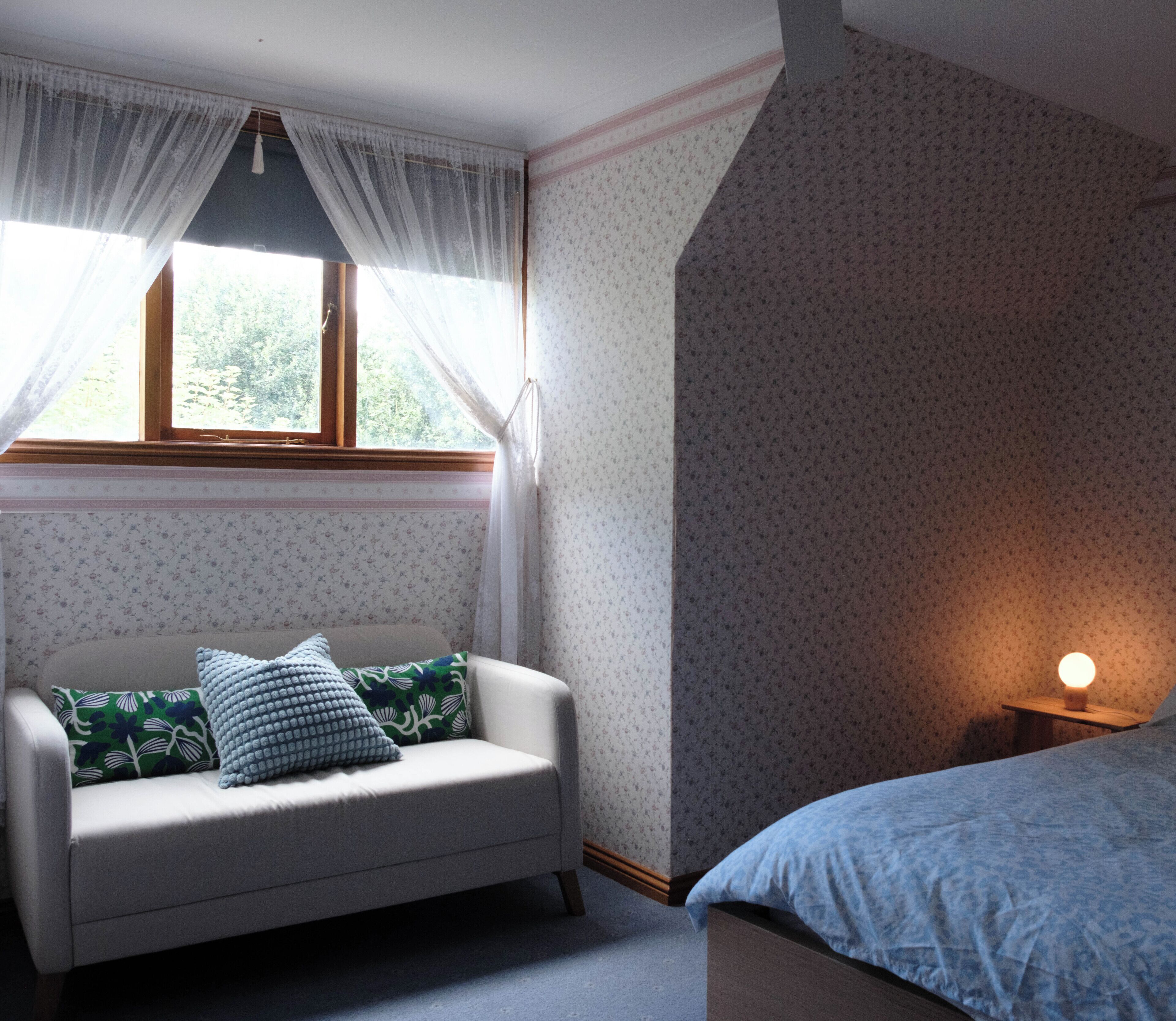 Una stanza con divano, letto, finestra con tende e lampada.