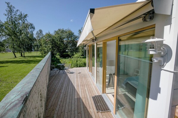 A covered outdoor deck with a glass door leading to a room.