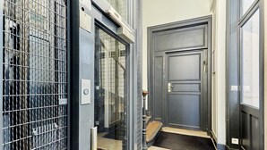 A narrow hallway with a metal gate, a wooden door, and a small step leading to a door with a doorknob.