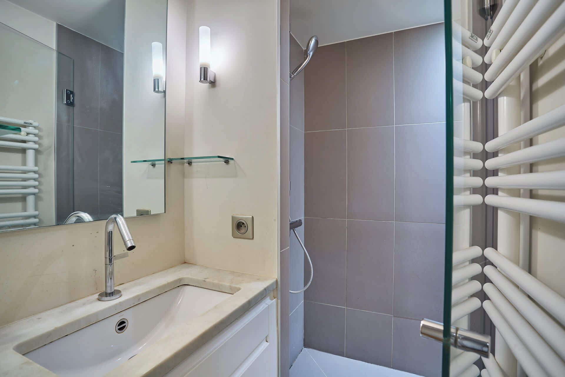 Une salle de bain équipée d’un lavabo, d’un miroir, d’une douche en verre et d’un porte-serviettes.