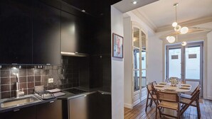 A modern kitchen with dark cabinetry and a dining area with a wooden table and chairs. - Elegant Appartment St Germain des Prés Invalides (Paris)