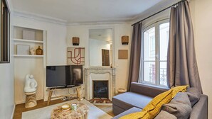 A living room with a fireplace, sofa, television, and decorative items. - Charming Apartment Center of Paris by Studio Prestige (Paris)