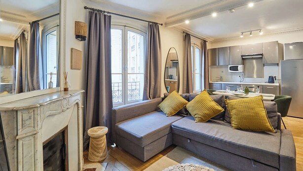 A modern living room with a grey sofa, yellow cushions, a fireplace, and a kitchen in the background. - Charming Apartment Center of Paris by Studio Prestige (Paris)