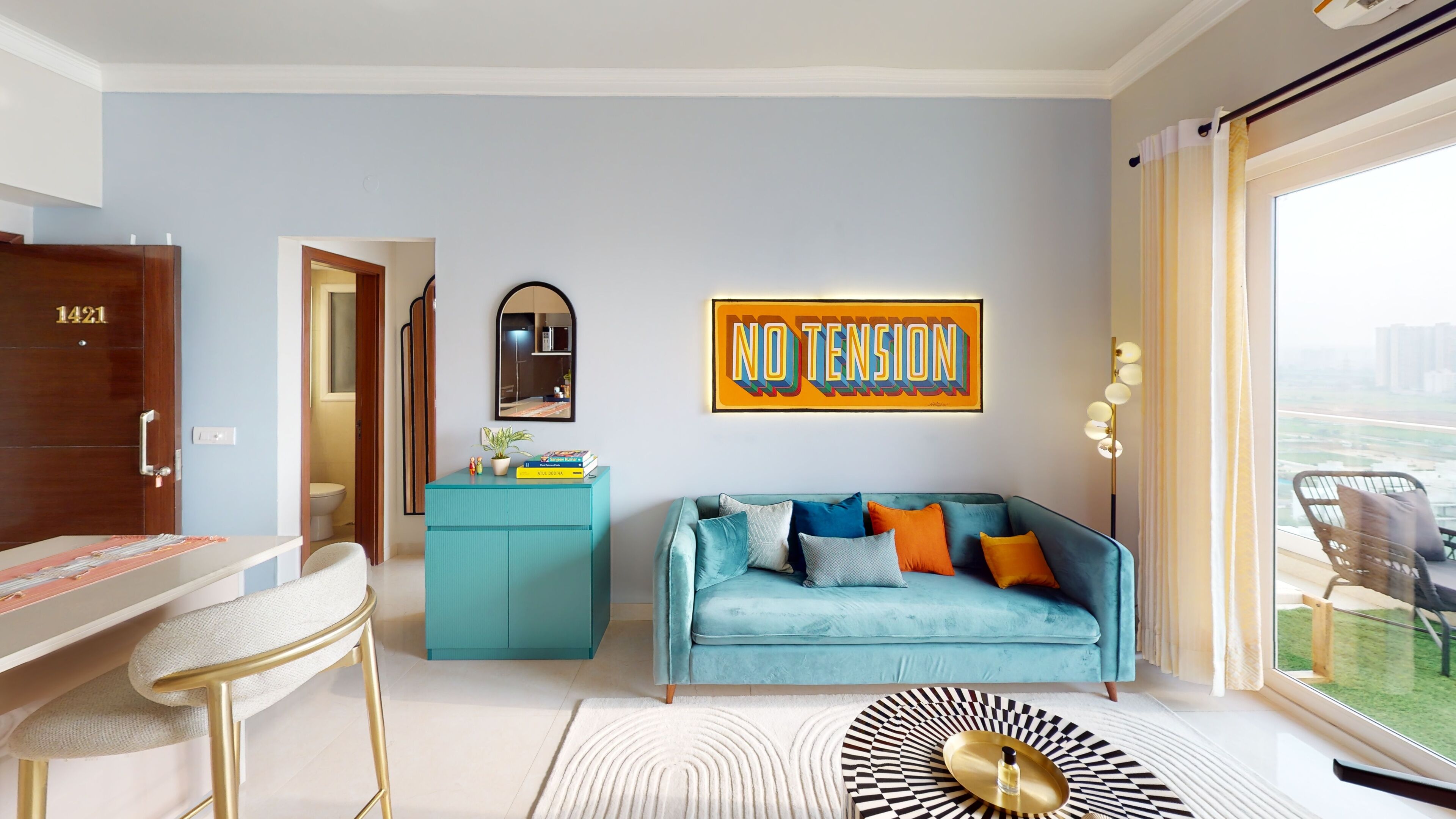 Un salon moderne avec un canapé de couleur turquoise, une table basse agrémentée d’un plateau décoratif, un meuble bleu et une grande fenêtre donnant sur des immeubles.