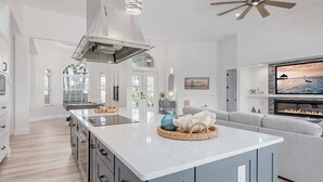 Una cocina moderna con una isla grande, un ventilador de techo y una chimenea en la sala de estar.