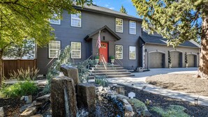 A house with a red door, a stone water feature, and a well-maintained garden. - New! Wildwood Manor ~ Salt Water Hot Tub ~ Dog Friendly ~ Fire Pit (Bend)