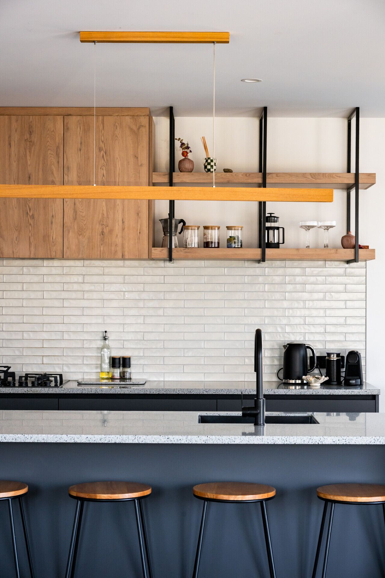 Uma cozinha moderna com armários de madeira, painel de backsplash de tijolo branco e um espaço bar com banquetas.