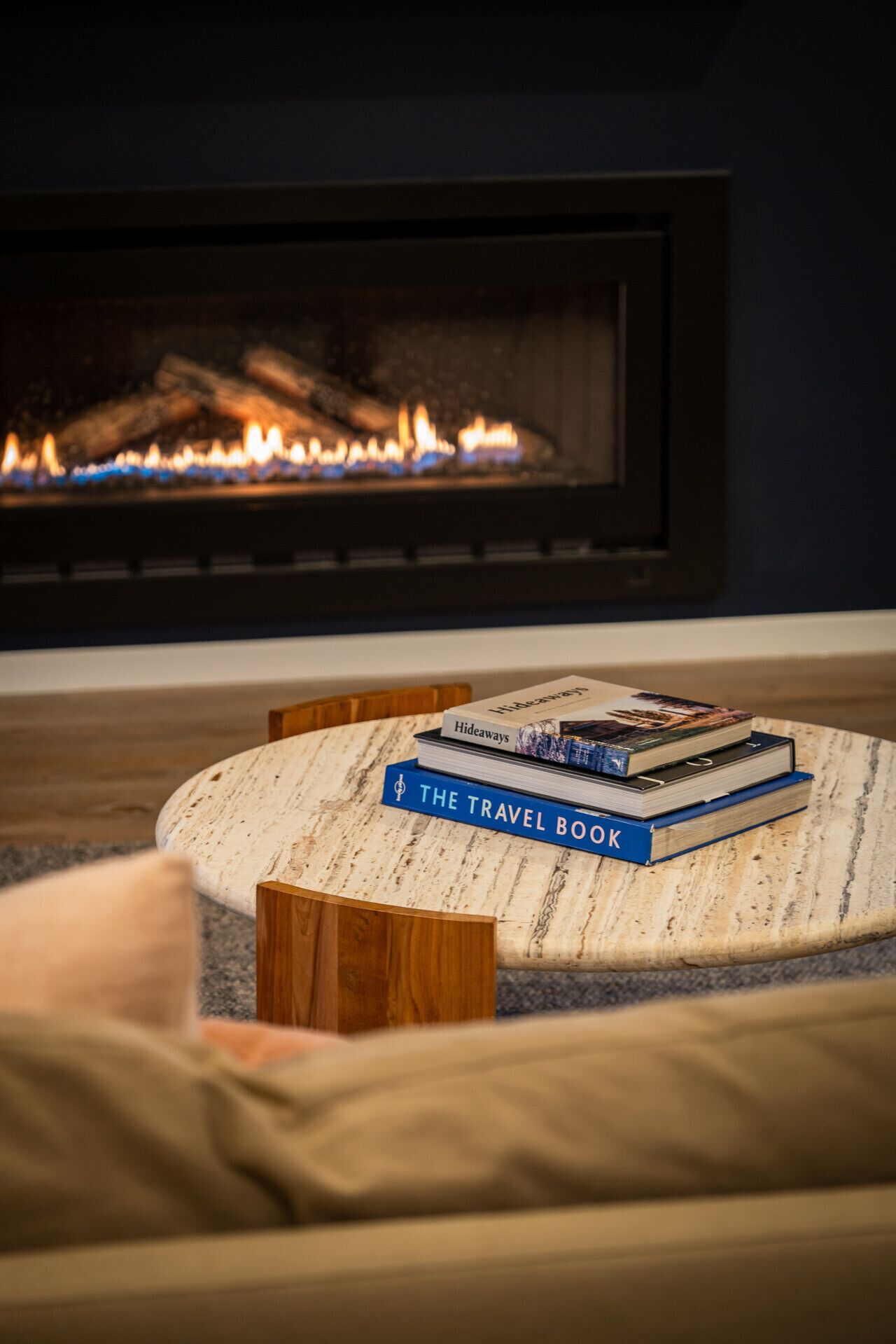 A cozy living room with a fireplace, a round coffee table with books, and a comfortable sofa.
