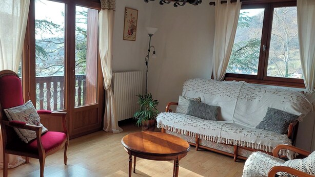 Een gezellige woonkamer met een rode fauteuil, een witte bank en een houten salontafel.