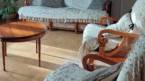 Een gezellige kamer met een houten plafond, een bank, twee schommelstoelen, een houten tafel en een raam met gordijnen.