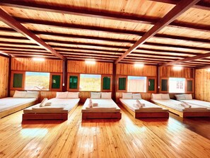 A room with wooden floors and walls, multiple beds arranged in rows, and windows with green curtains. - Duong Thuong - Eco House (Duong Thuong)