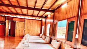 Une rangée de lits superposés en bois, avec des oreillers, un plancher en bois et de grandes fenêtres.