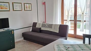 En stue med sofa, bord og fjernsyn. Der er indrammede billeder på væggen og en rød stang.