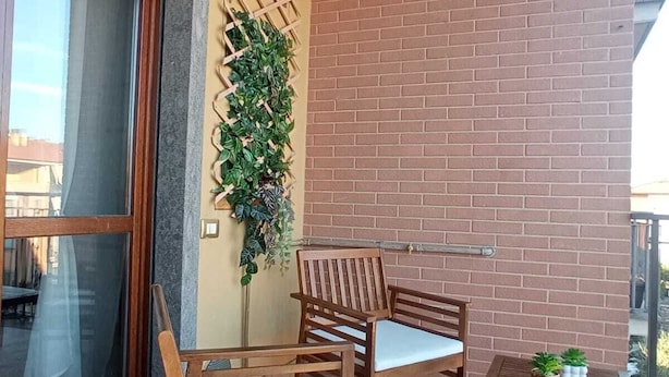 A balcony with two wooden chairs and a small table, a potted plant, and a brick wall.