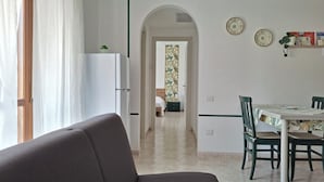 A modern living room with a sofa, a dining table with chairs, and a kitchen area with a refrigerator.