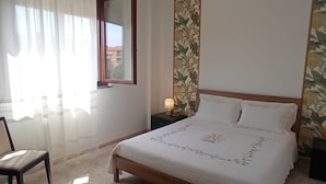 A bedroom with a bed, a chair, a nightstand, and a window with curtains.