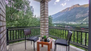Ein Balkon mit zwei Stühlen, einem Tisch und einer Säule mit Fliesen, mit Blick auf eine gebirgige Landschaft.