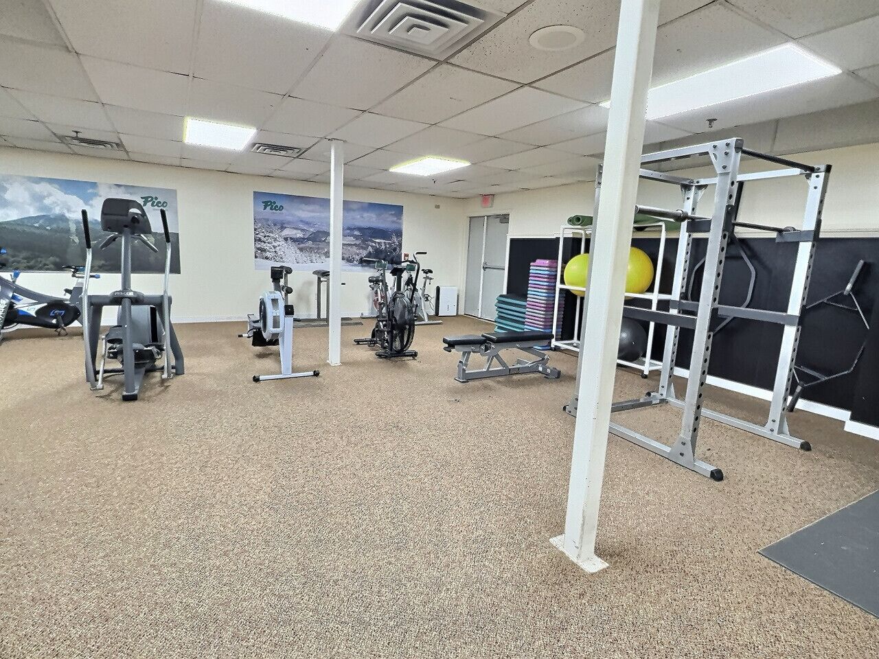 Une salle de sport équipée de divers appareils d’entraînement, notamment un banc de développé couché, des haltères et un support à squats.