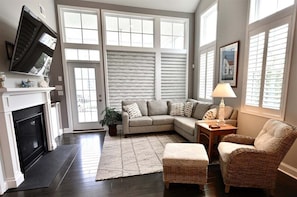 A living room with a fireplace, a sofa, a chair, a lamp, and large windows.