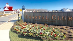 Schild des Coastal Club, Geschwindigkeitsbegrenzung von 40 km/h, ein Leuchtturm und ein gepflegter Blumenbeet.