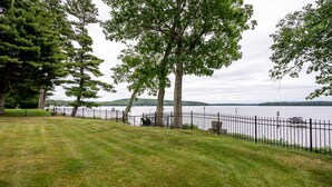 A grassy area with a fence and trees, overlooking a body of water. - Winnipesaukee waterfront escape with private dock and guest cottage (Tuftonboro)