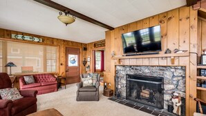 A cozy living room with a stone fireplace, wooden walls, a television, and comfortable seating. - Winnipesaukee waterfront escape with private dock and guest cottage (Tuftonboro)
