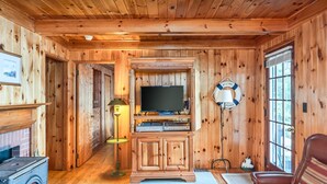 Et interiør af en træhytte med en pejs, et fjernsyn på et træskab, en lampe og en læderstol.