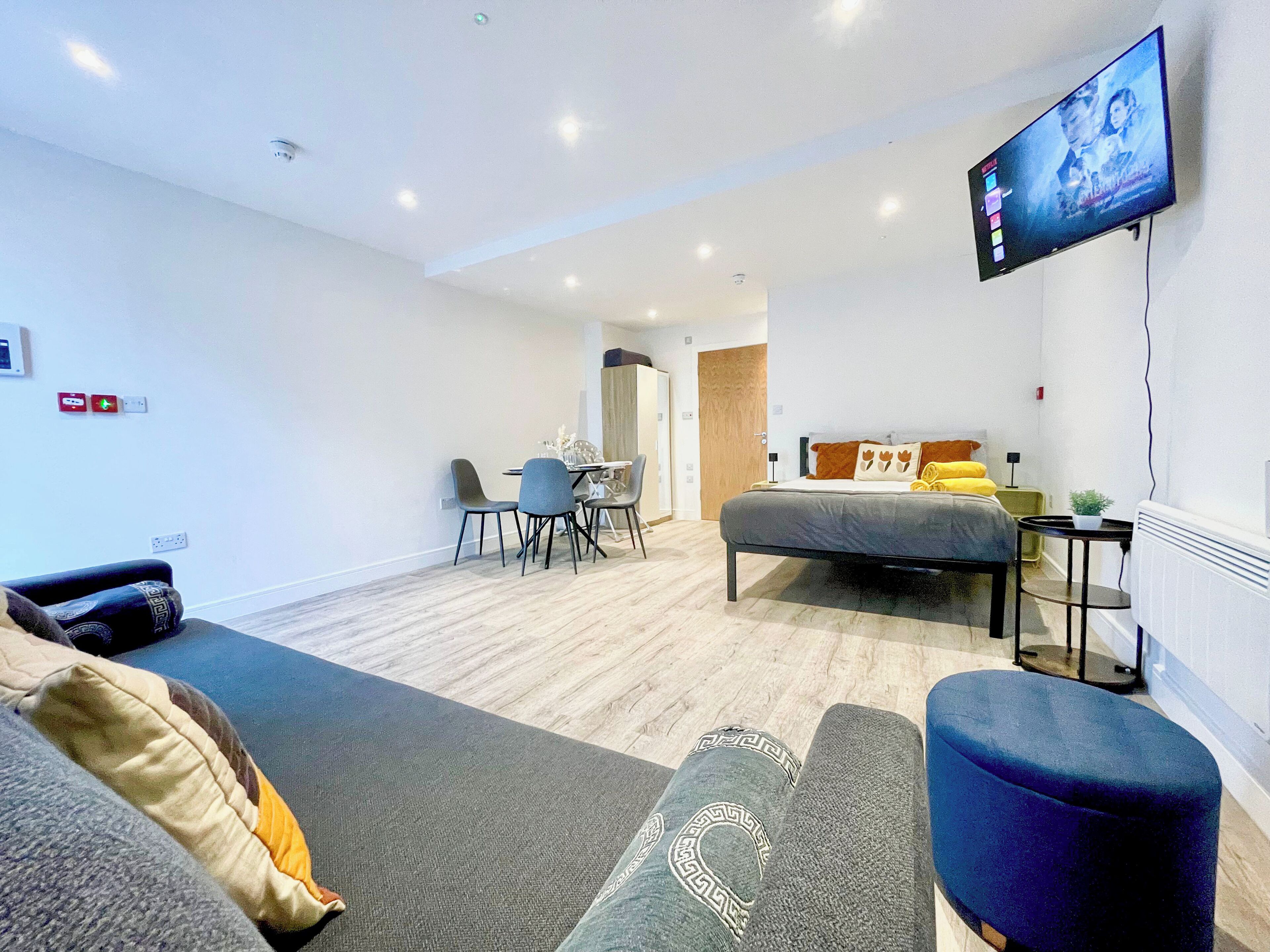 Ein modernes Hotelzimmer mit Bett, Wandfernseher, Essbereich mit Stühlen und einem kleinen Tisch.