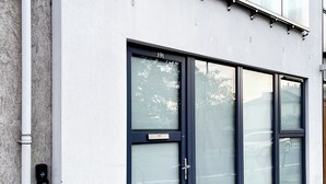 A modern building facade with large glass windows, a door with a number plate, and a security keypad.