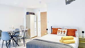A modern hotel room with a bed, bedside tables, a desk with chairs, and a wardrobe.