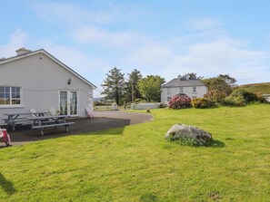 A white building with a patio area, outdoor seating, and a large rock in the foreground.