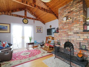 A cozy living room with a brick fireplace, wooden ceiling beams, a clock, and a comfortable seating area.
