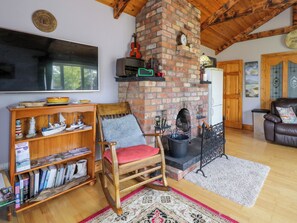 A cozy living room with a brick fireplace, wooden furniture, a bookshelf, and a television.