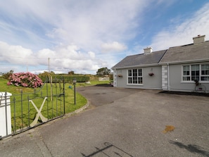 A building with a paved entrance, a white fence, and a garden with pink flowers.