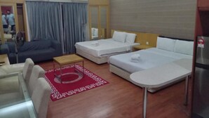 A hotel room with a sofa, two single beds, a small table, and a red patterned rug. - Maytower Service Studio Apartment (Kuala Lumpur)